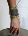 A close-up of a person's forearm and hand wearing a knitted wrist cuff in gray and yellow, resting against a white fabric-covered surface.