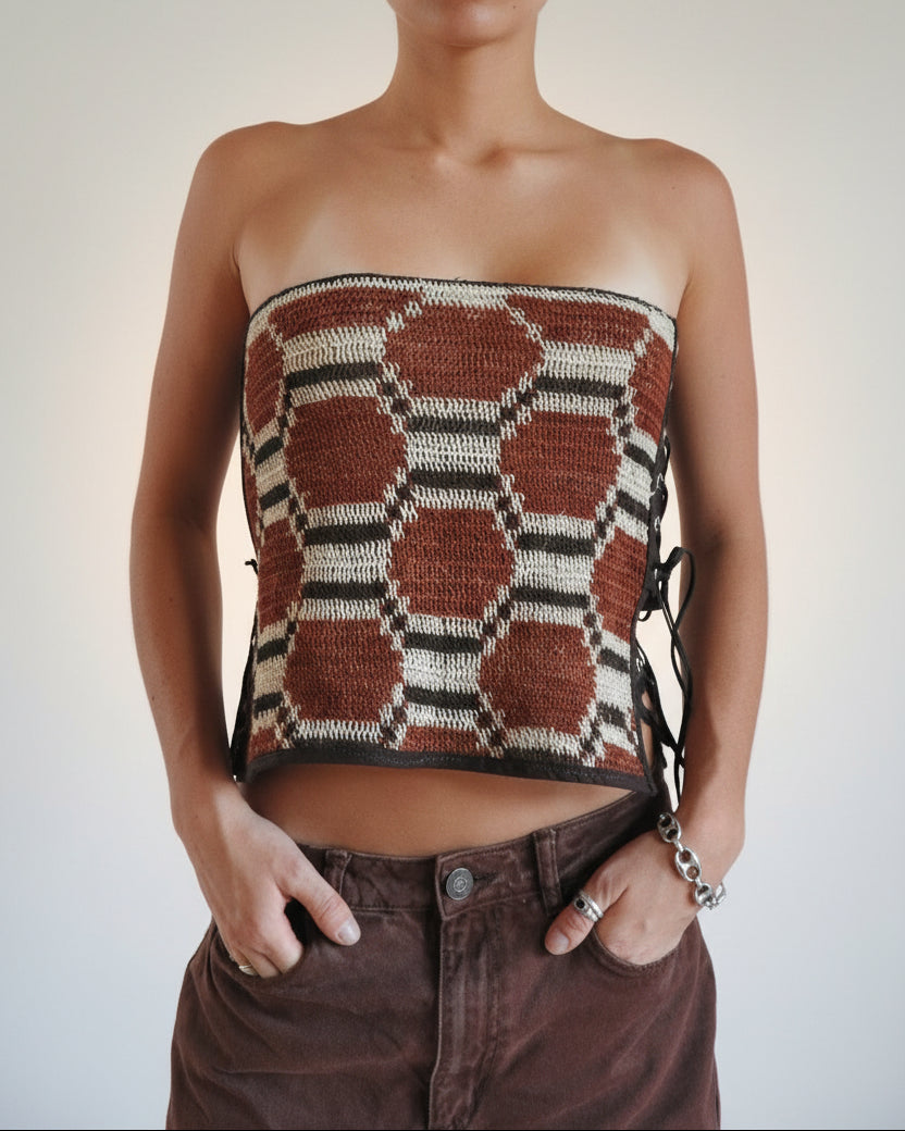 A person wearing a strapless knit tube top with a geometric hexagon pattern in brown, beige, and black, paired with brown corduroy pants.